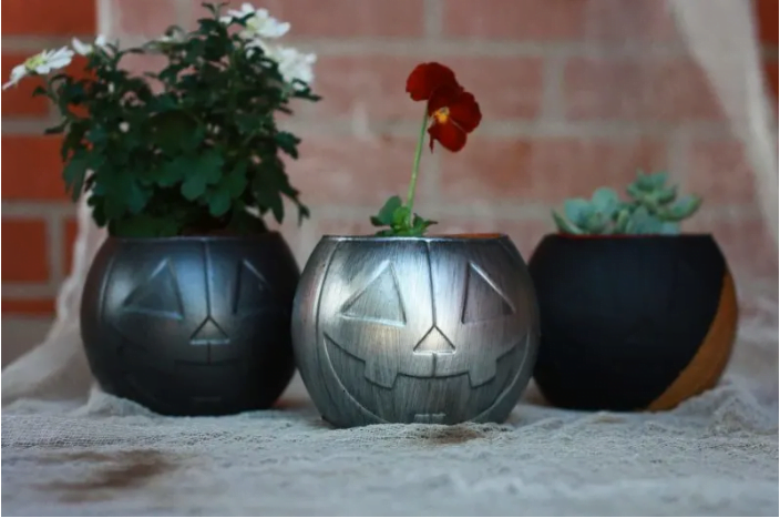 Three plastic pumpkin buckets painted silver and black and filled with live plants